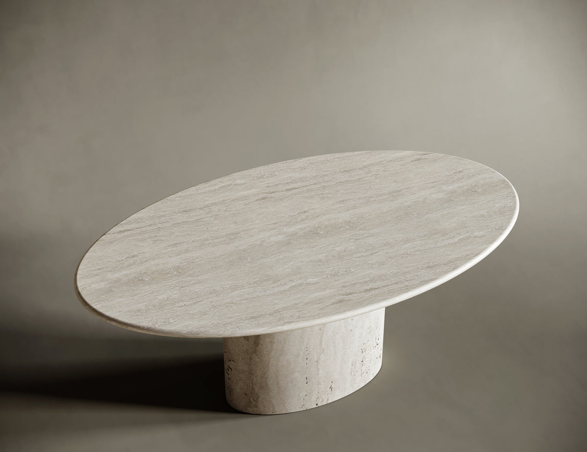 Elliptical travertine coffee table with a matching pedestal base, set against a seamless taupe background. The table's natural stone texture and warm beige tones are accentuated by soft lighting, creating a sophisticated and minimalist aesthetic. Perfect for modern interiors and vintage luxury furniture enthusiasts