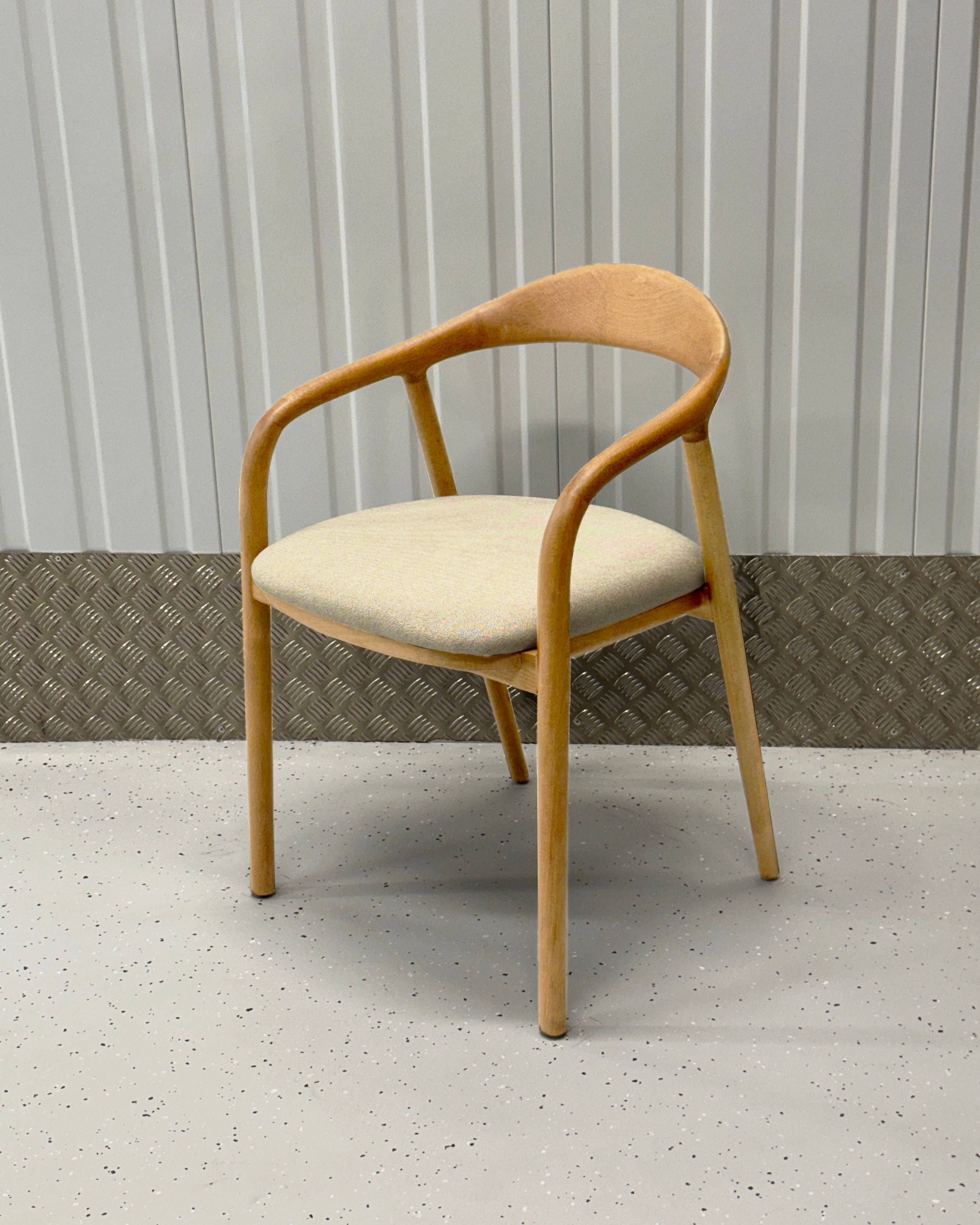 A beige upholstered padded seat on a wooden dining chair with a full backrest and armrests, placed against a textured background.