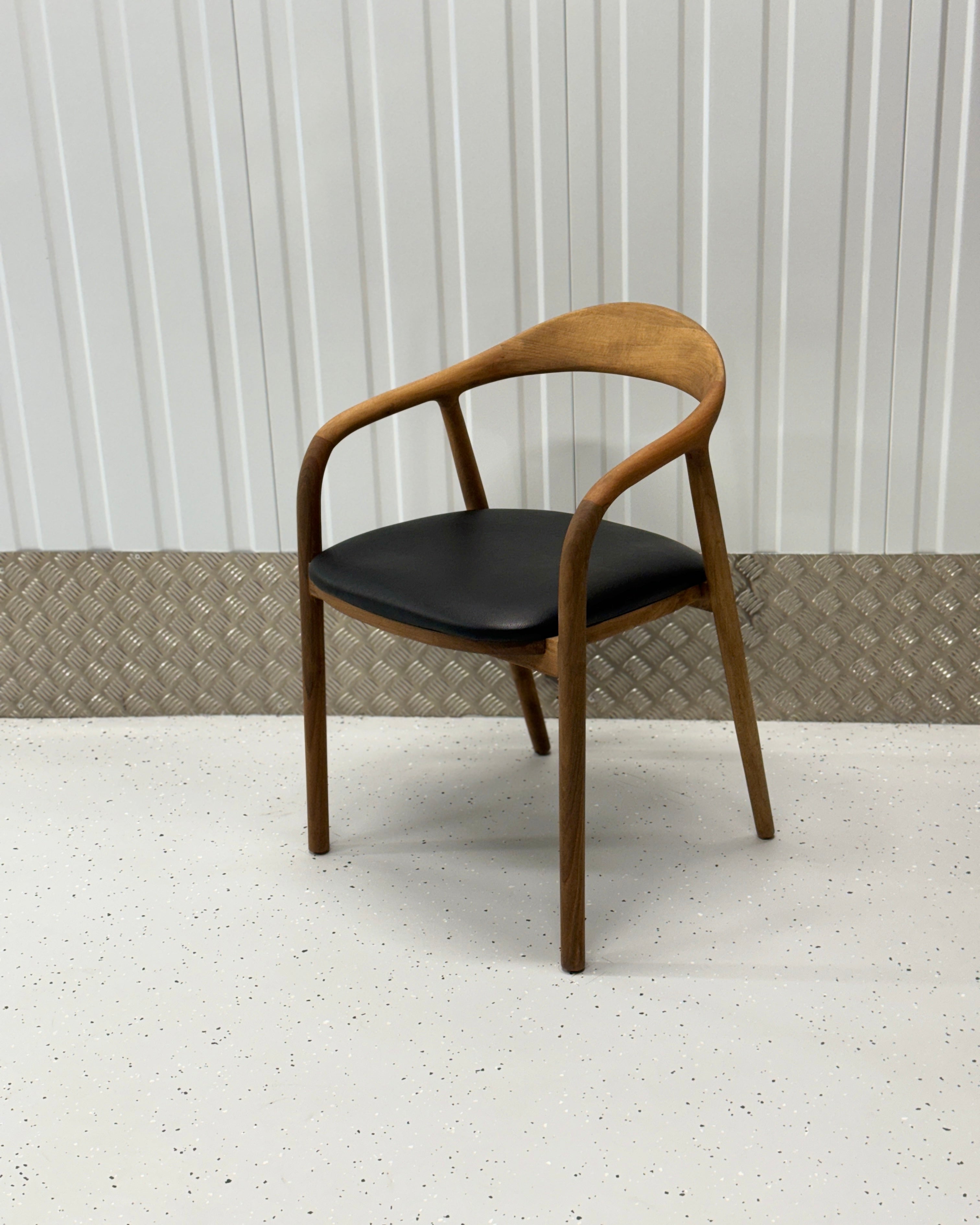 A walnut wood dining chair with a black seat cushion, showcasing a curved backrest and armrests.