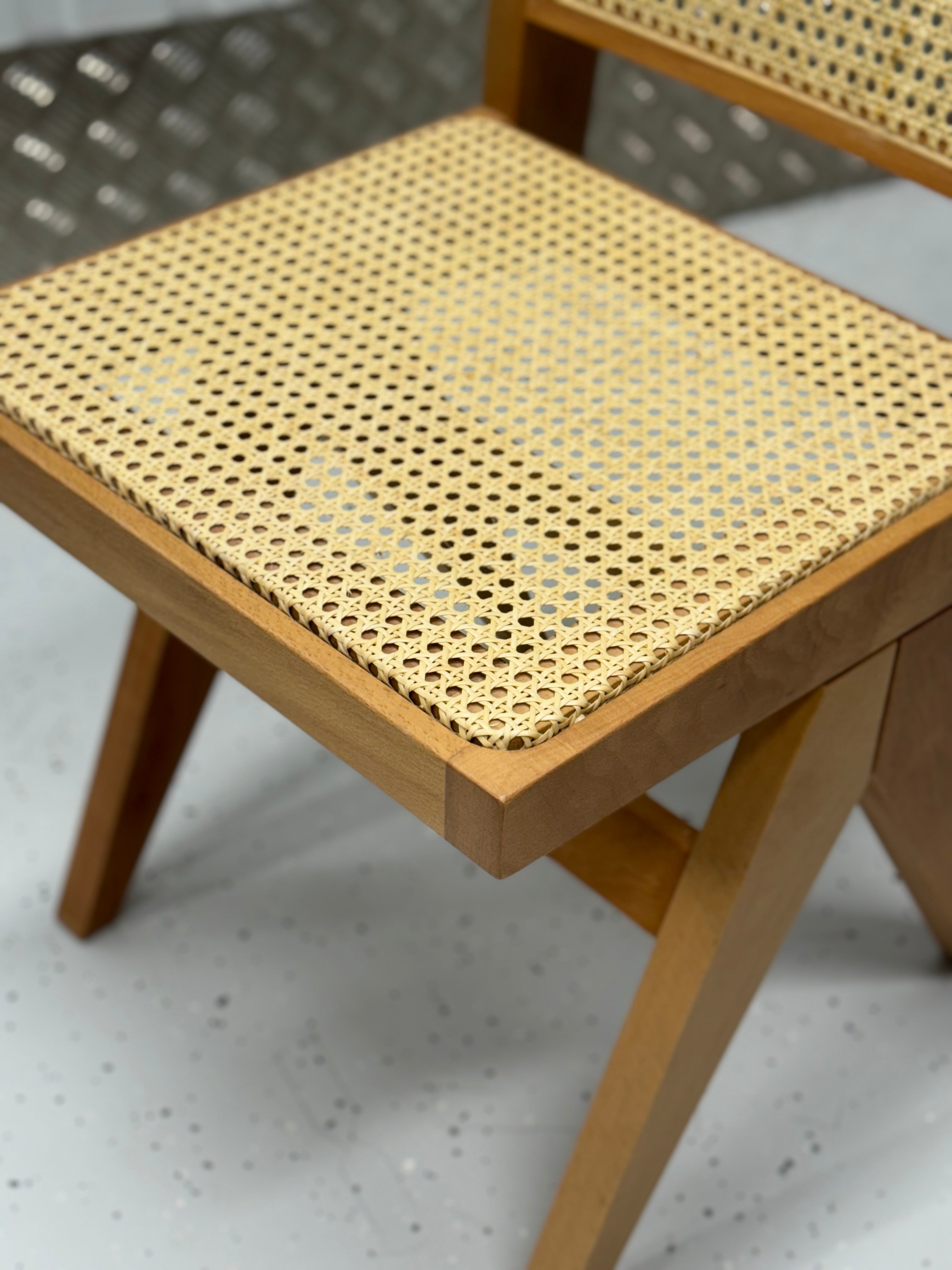 Pierre Jeanneret-inspired chair with a refined wooden frame and airy rattan details, ideal for creating a sophisticated yet relaxed dining atmosphere.