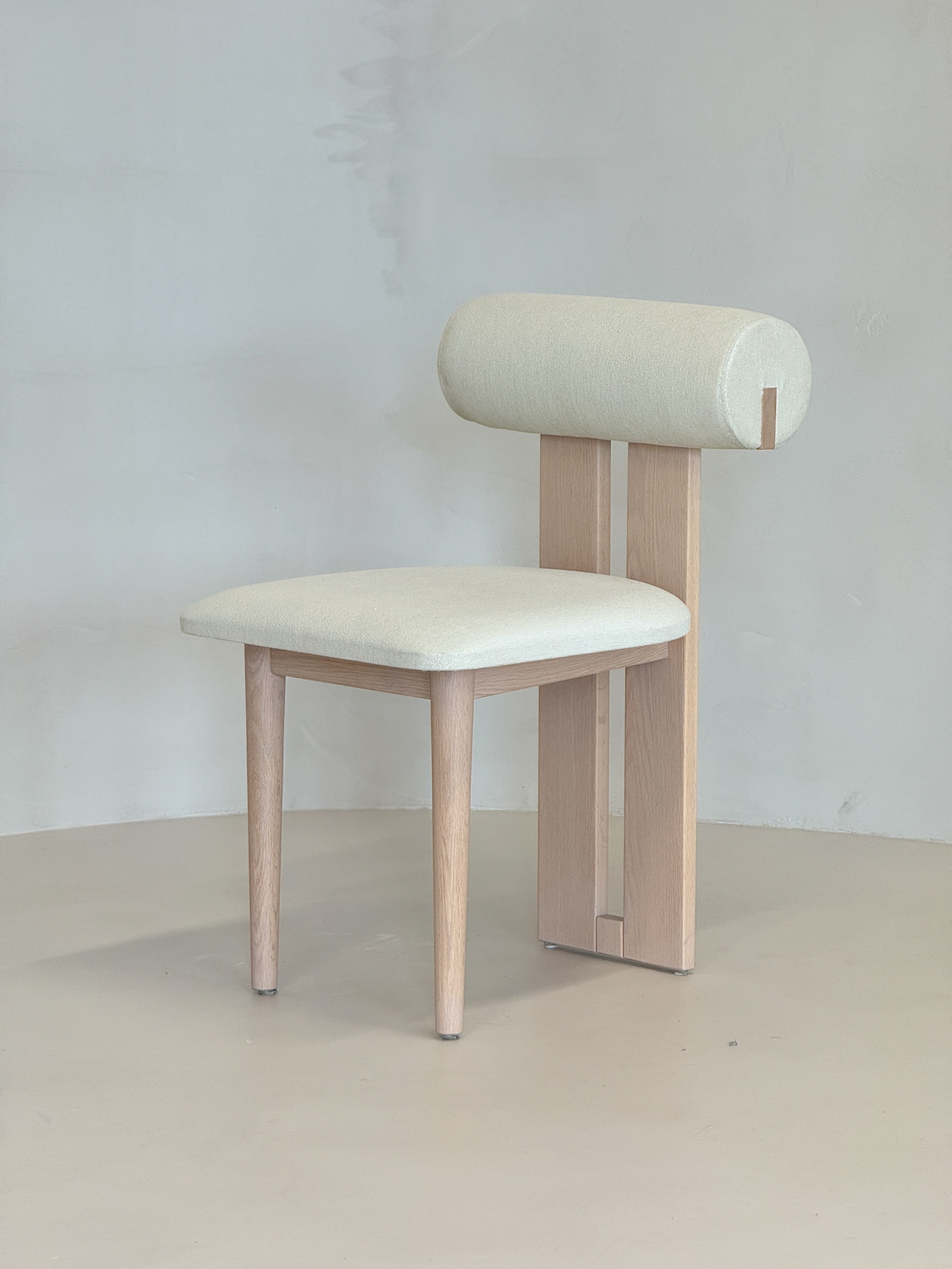 wooden "Roll Chair by BEDÚ Atelier featuring a cylindrical backrest and solid wood frame, perfect for modern dining spaces."