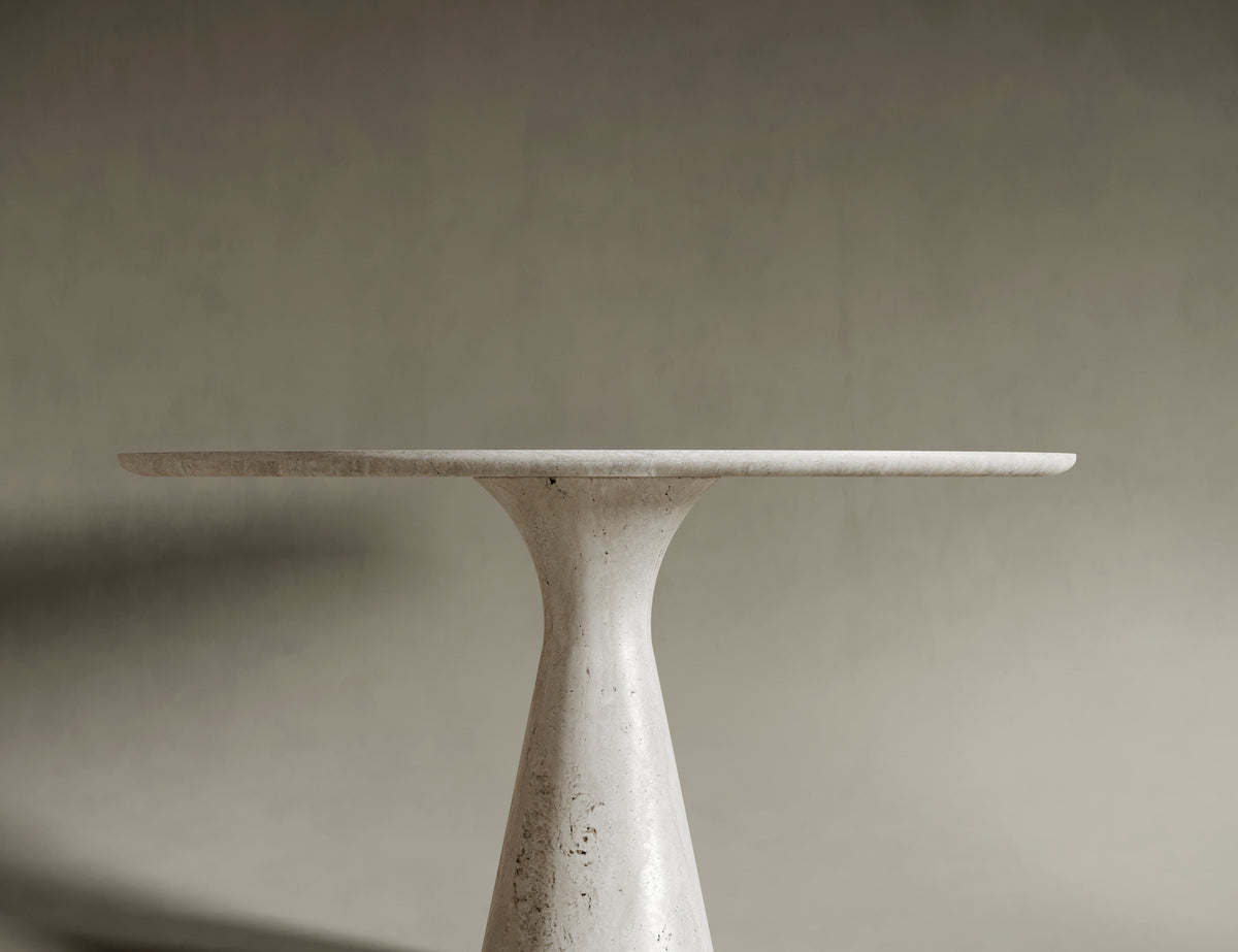Close-up of a round travertine tabletop, emphasizing its natural stone texture, soft veining, and honed finish. The light beige surface reflects the organic beauty and artisanal quality of the material, perfect for sophisticated interiors