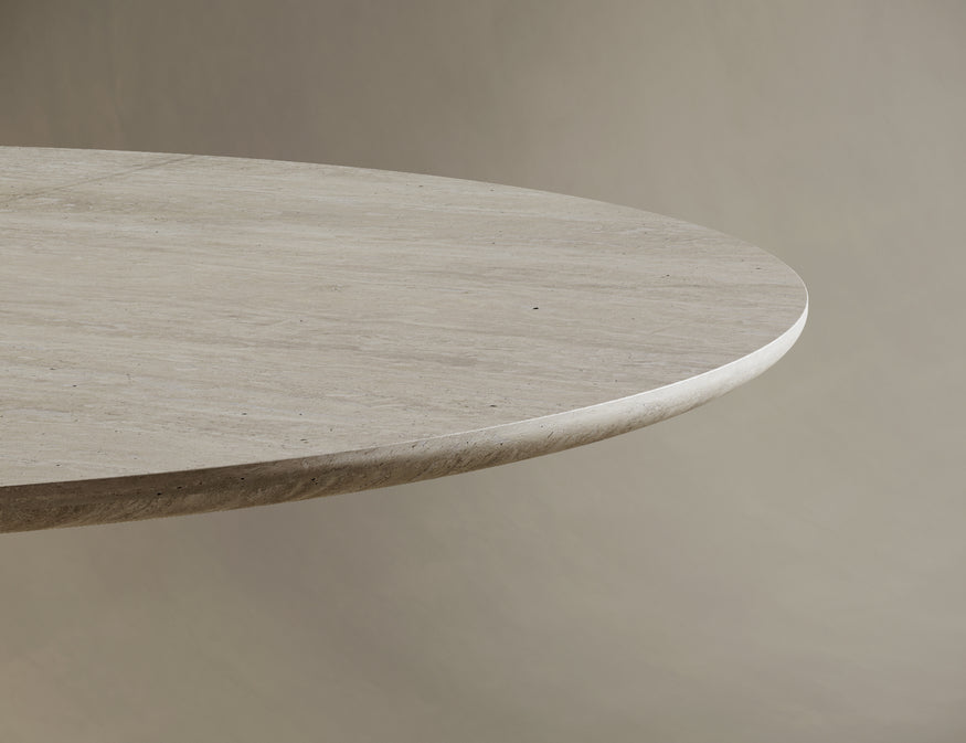 Round travertine dining table adorned with a matching stone vase holding dried twigs and unlit pillar candles. The natural materials and minimalist decor create a serene and luxurious dining atmosphere, blending organic beauty with contemporary design.