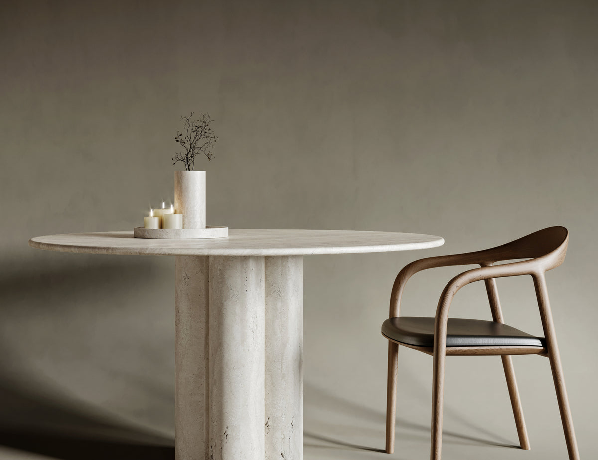 Elegant dining room featuring a round travertine dining table with four cylindrical legs. The natural stone surface showcases unique textures and organic patterns, creating a harmonious blend of modern design and timeless craftsmanship.