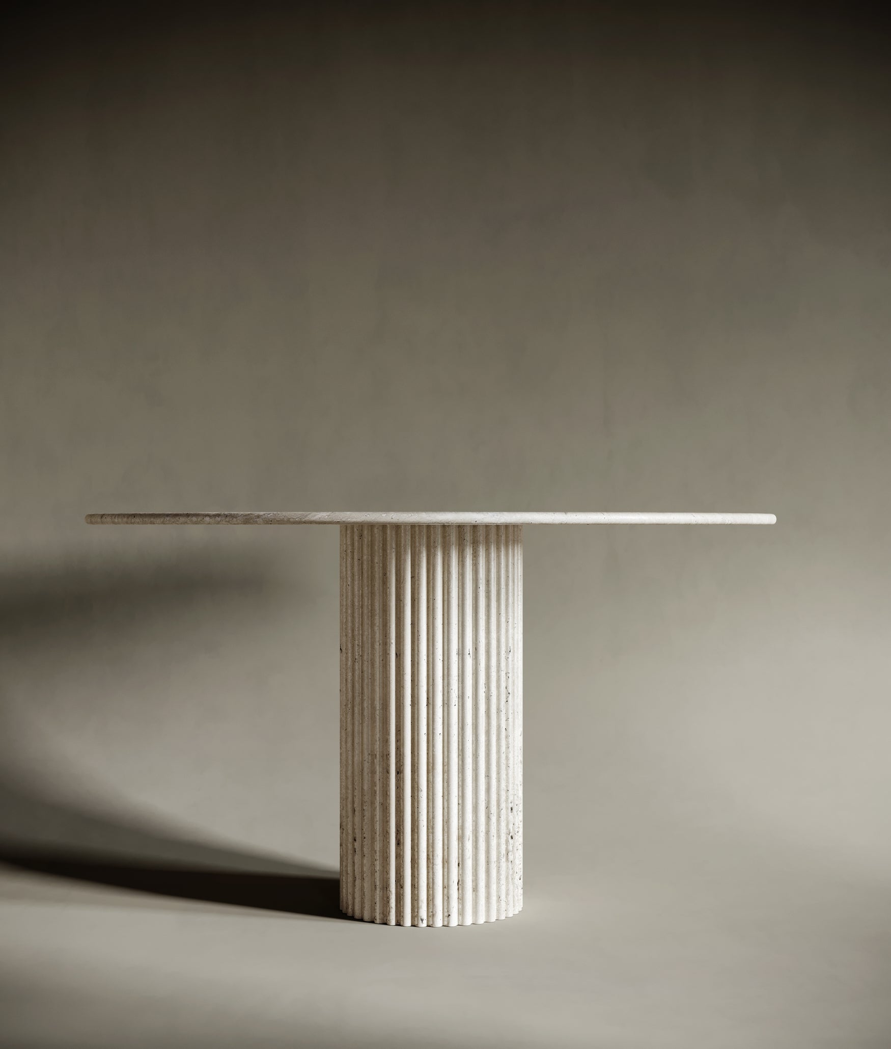 The Round Travertine Dining Table by BEDÚ Atelier, featuring a hand-carved, sculptural fluted leg as its base.
