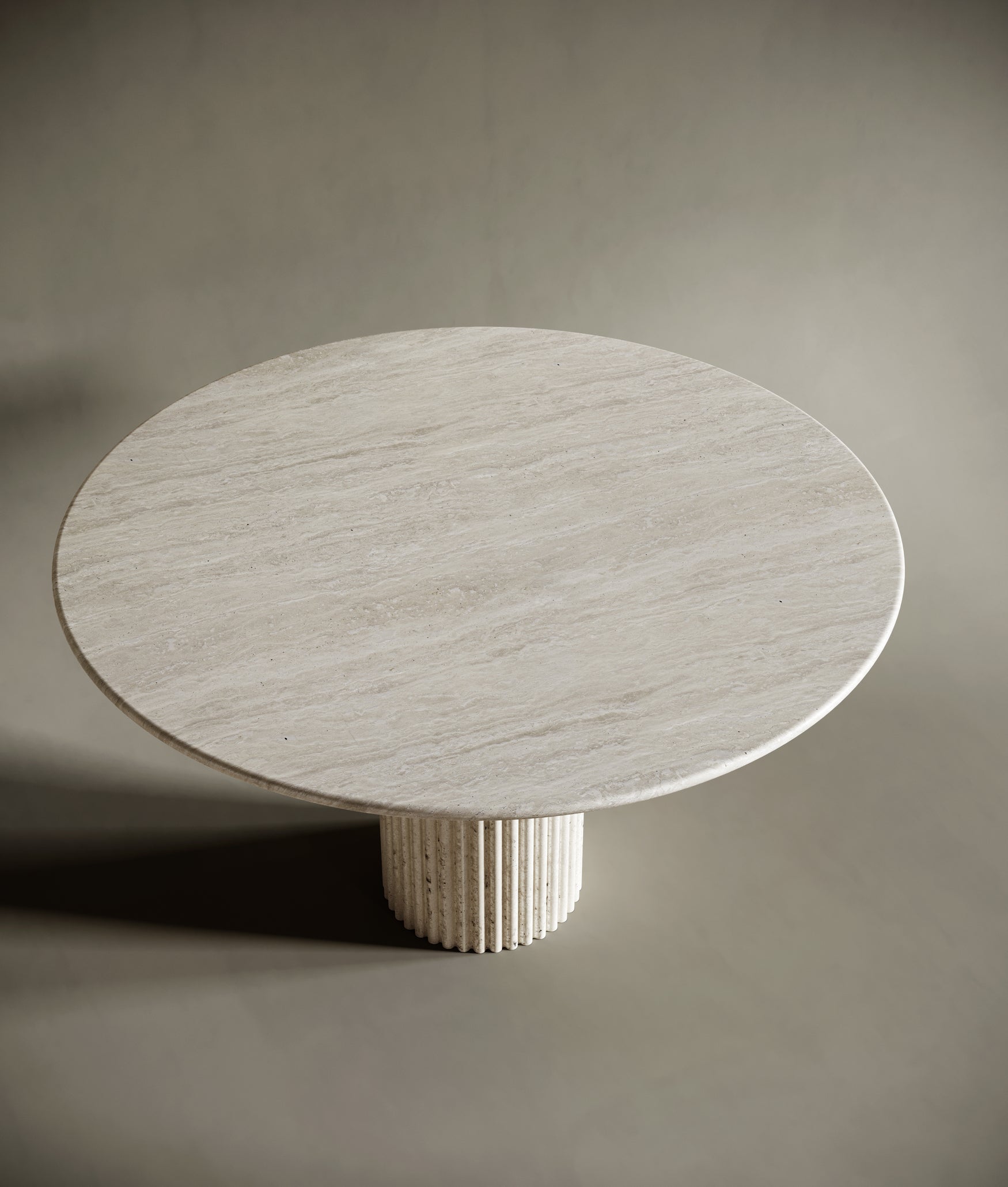 BEDÚ Atelier's Round Travertine Dining Table with its unique fluted leg, creating a sophisticated centerpiece in a neutral room.