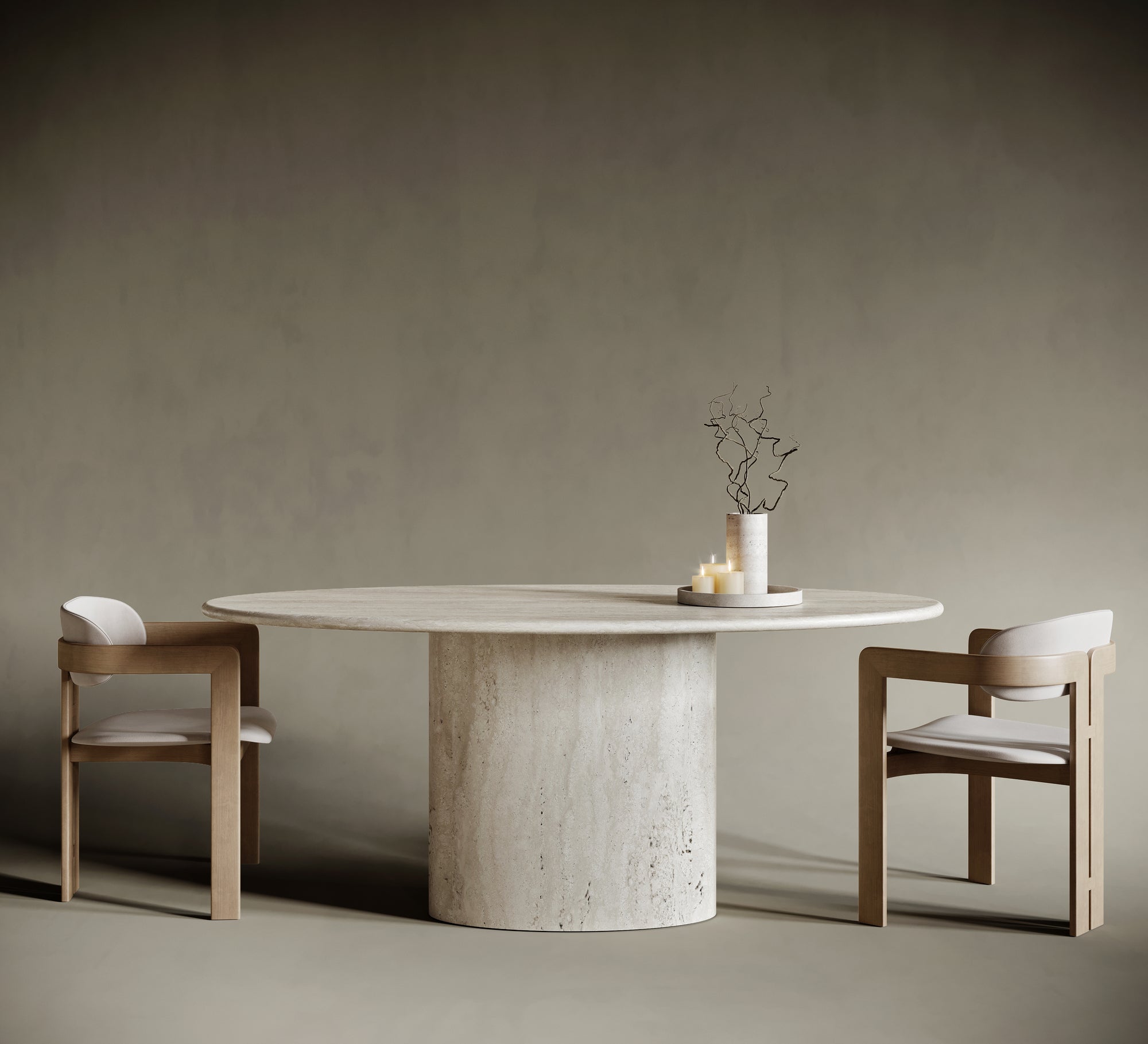 Minimalist dining room featuring a round ellipse travertine dining table with a cylindrical pedestal base, paired with two modern wooden chairs upholstered in cream fabric. The natural stone table showcases a textured surface, complemented by a simple centerpiece of twisted branches and candles. Set against a muted taupe background, this elegant interior highlights contemporary furniture design and natural materials