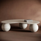 FABIO travertine coffee table with a free-form, flowing top and sculptural spherical bases, showcasing natural stone textures.

