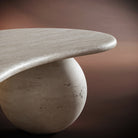 MARCO travertine coffee table set against a warm brown background, emphasizing its organic form and timeless design.