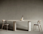 Oval travertine dining table with a bold semi-cylindrical leg, marrying traditional stone craftsmanship with modern sculptural aesthetics; smooth honed surface and soft stone hues create a harmonious centerpiece for refined interiors.