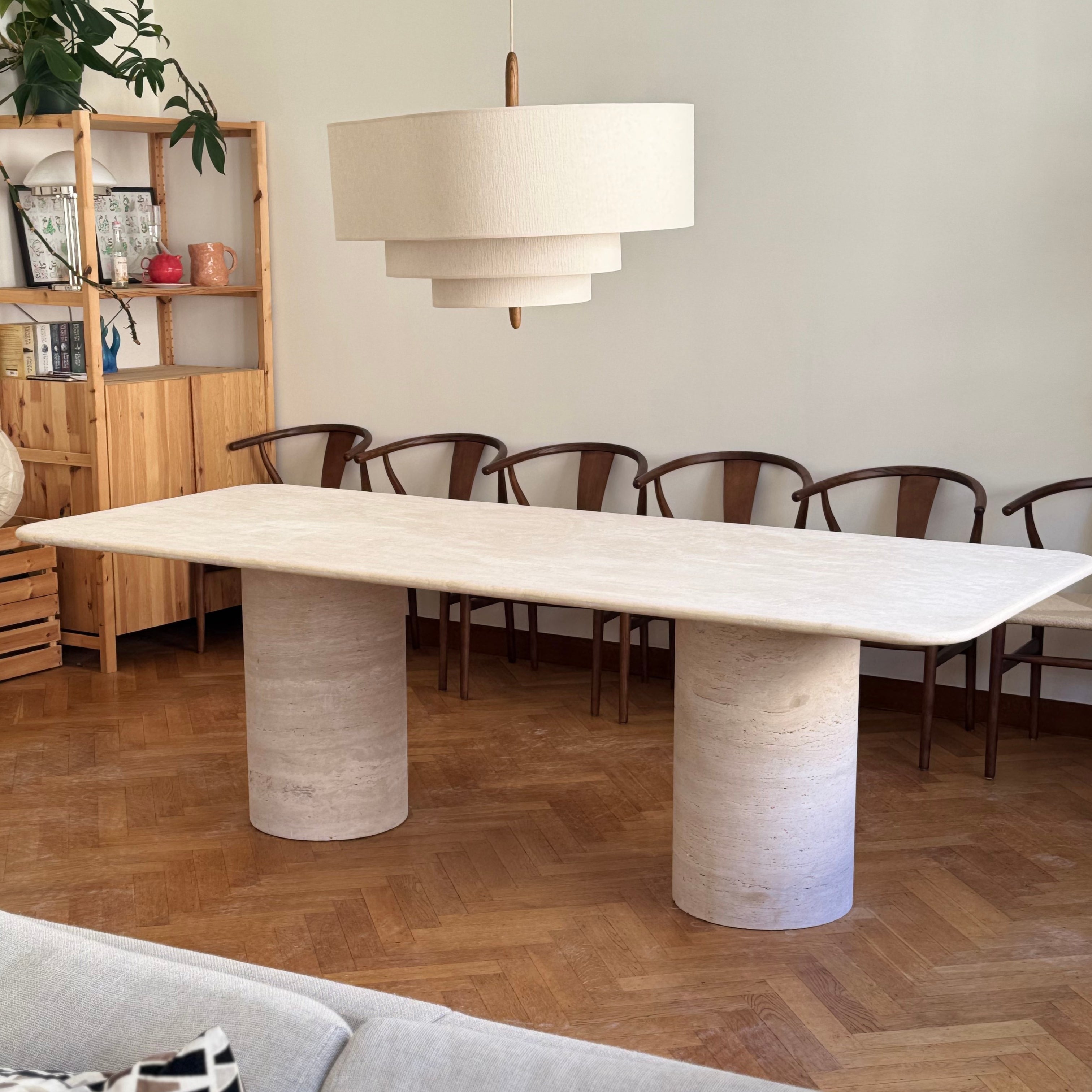 Dining room with a large marble table on cylindrical legs, wooden chairs, and a lamp.