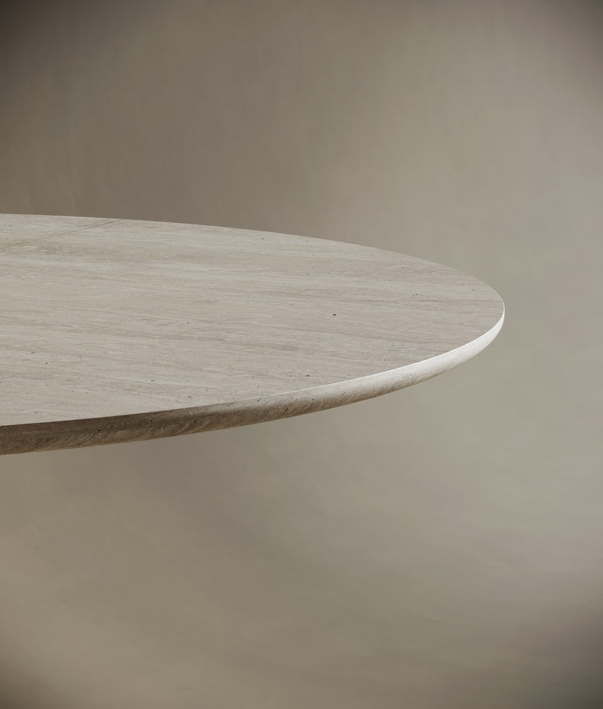 Round travertine dining table adorned with a matching stone vase holding dried twigs and unlit pillar candles. The natural materials and minimalist decor create a serene and luxurious dining atmosphere, blending organic beauty with contemporary design.