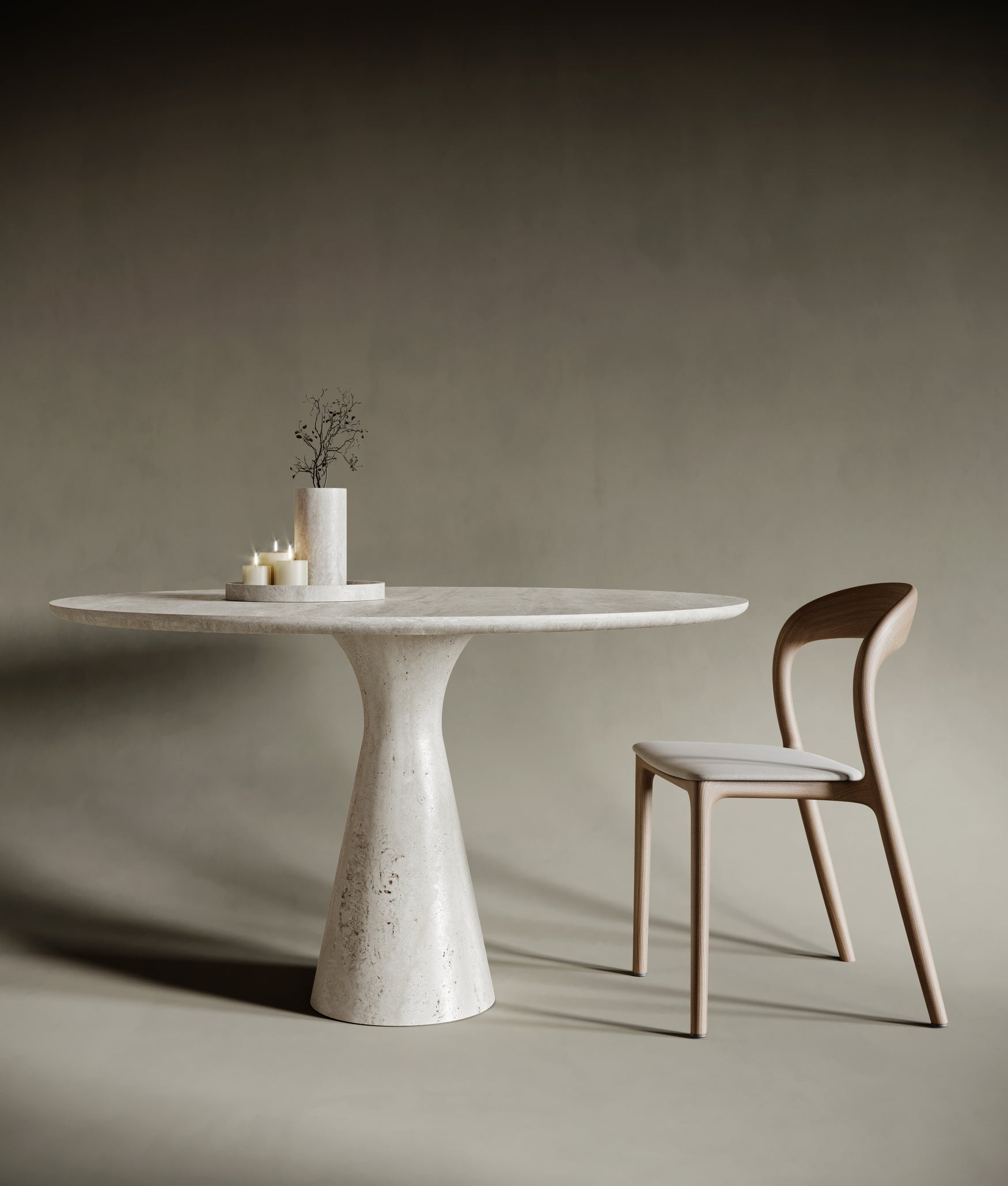 Minimalist dining room featuring a round travertine dining table with a sculptural curved leg. The natural stone surface showcases unique textures and subtle veining, paired with a light wooden chair. Set against a muted taupe background, this elegant design highlights timeless craftsmanship and modern luxury.