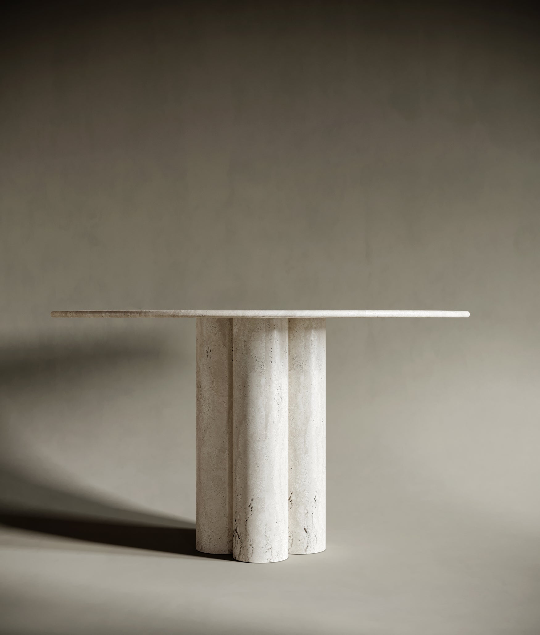 Detailed view of the four cylindrical travertine legs of a round dining table, showcasing their sculptural elegance and solid craftsmanship. The natural stone texture adds depth and character to this luxurious design.